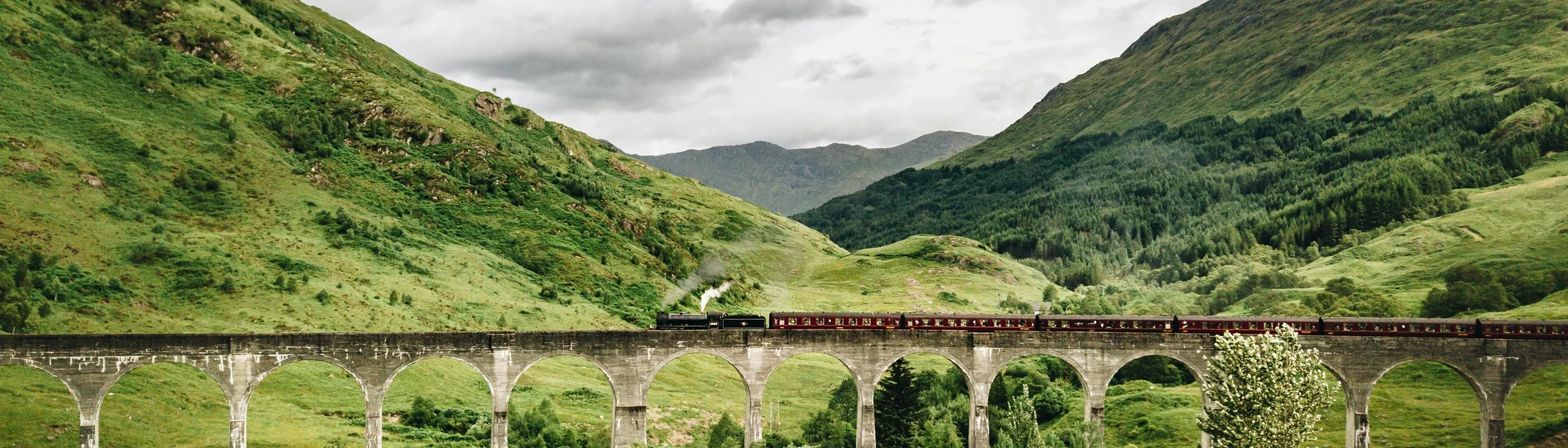 Train crossing the curved Glenfinnan Viaduct amid green Highland hills on the West Highland Line